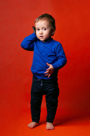 A pretty toddler boy with smartphone imitates a phone conversation.