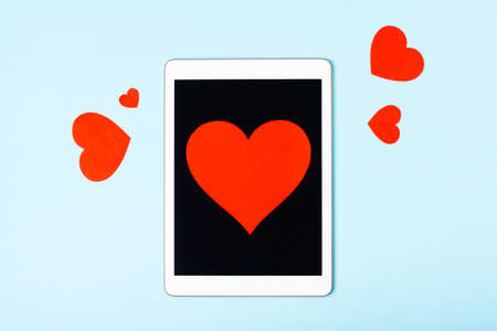 Tablet on a blue background with cute hearts. The concept of meeting website, love in internet, love to your gadget and technology, love correspondence, Valentines Day, surprise. Flat layの写真素材