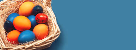 Banner with Easter eggs in orange and blue colors in a basket. Copy space. The concept of stylish...