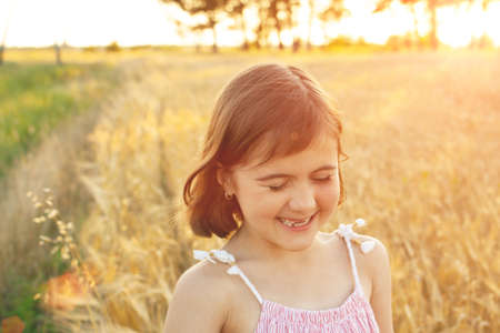 Funny girl laughs on a walk across the field at sunset. The concept of real childhood, digital detox, summer vacations, happiness.の写真素材