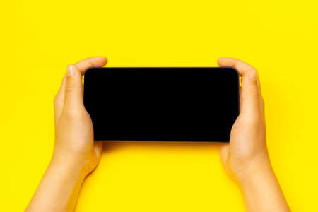 Smart phone with childs hands on the yellow backstage. The concept of necessary things of a little...