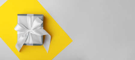 Trendy attractive minimalistic gift on the yellow and gray background. Colors of 2021. Merry...