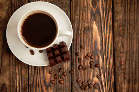white cup of coffee and chocolate,beans on the brown wooden background