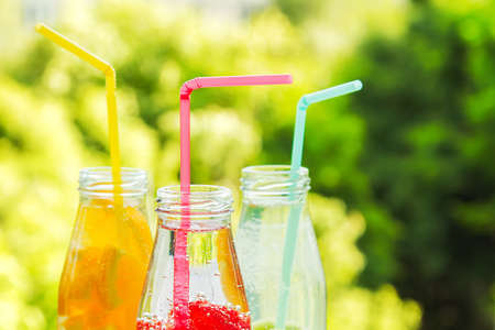 three ice cold fruit drinks in glass bottles ,summer garden in the backgroundの写真素材