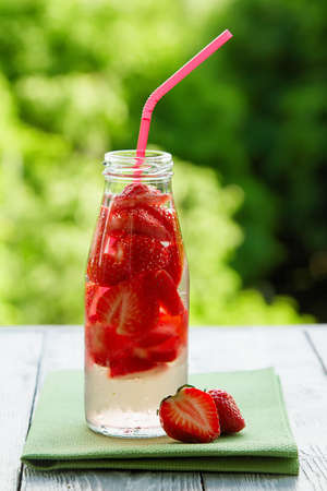 cold fresh strawberry drink in a bottle on wooden grey table in the summer gardenの写真素材