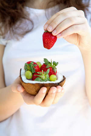 Healthy diet. Woman hands holding dessert of strawberries and grapes in half coconutの写真素材