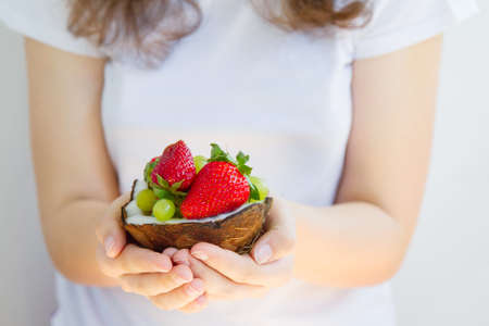 Healthy diet. Woman hands holding dessert of strawberries and grapes in half coconutの写真素材