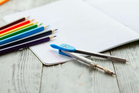 an open notebook on a wooden table lay next to colored pencils and compasses. School Desk mess