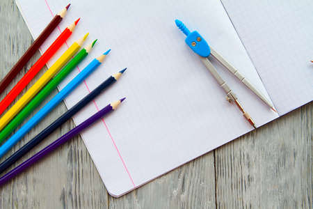 an open notebook on a wooden table lay next to colored pencils and compasses. School Desk mess,top view.の写真素材
