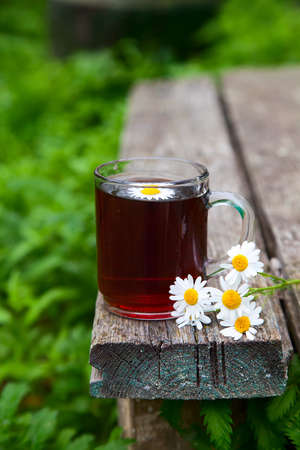 a bouquet of chamomile flowers and herbal tea on a wooden old background in the garden. Rustic still lifeの写真素材