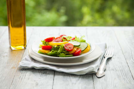 summer vegetable salad with olive oil on a wooden background next to a glass bottle of oil. Natural summer backgroundの写真素材