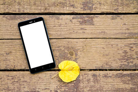 black mobile phone on a wooden old autumn background, near the yellow autumn leaf.Copy spaceの写真素材