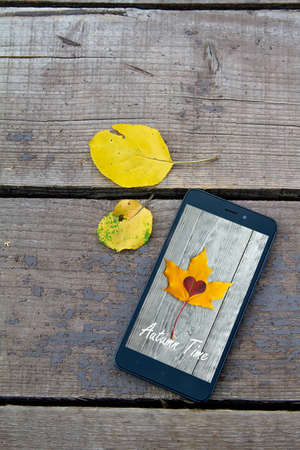 black mobile phone on a wooden old autumn background, near the yellow autumn leaves.Copy spaceの写真素材