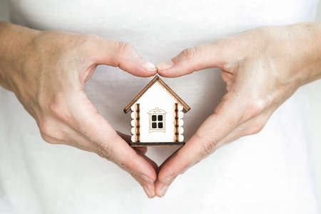 hands in the form of hearts holds a small white wooden house of cards. Close up.の写真素材