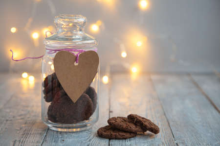 glass jar with chocolate chip cookies on grey wooden background with glowing garland and paper heartの写真素材