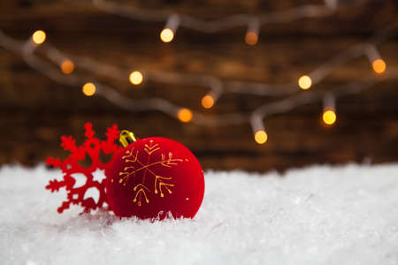 Christmas red ball on a snowy and wooden background. Festive bokeh from lights garlandの写真素材