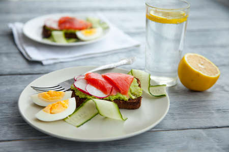 Two smorrebroad sandwiches with red fish,Avocado,eggs and cucumber on plate on a table. Healthy breakfast or lunch.の写真素材