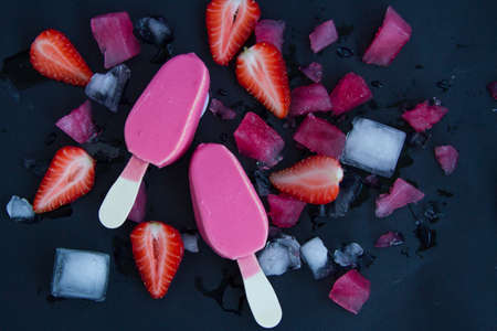 two pink ice cream on a black background next to the sliced strawberries and chopped ice. Summer...