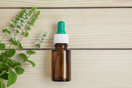 one bottle of peppermint essential oil and fresh mint of brunch on wooden background