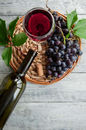 A cluster of dark grapes and wine glass,bottle on a round straw tray and grey wooden table,top view and copy space.の写真素材
