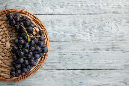A cluster of ripe dark grapes on a round straw tray. Top view and copy spaceの写真素材