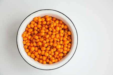Handful of useful medicinal sea buckthorn berries in a white bowl on a white isolated background.