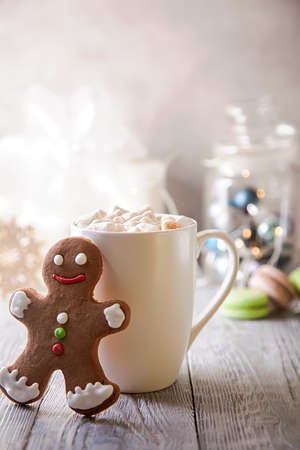 White mag of coffee with marshmallow and gingerbread snowman on a wooden table. Christmas break .