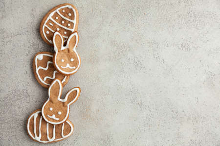Easter decorated cookies in the shape of a bunny and eggs are laid out in a row on a gray...