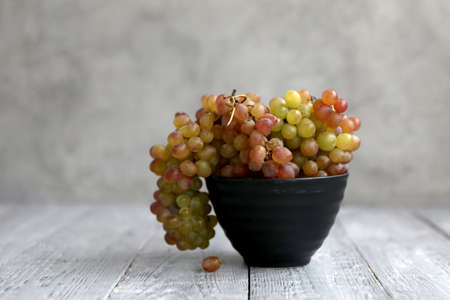 Still life with colored grapes in a black bowl on a gray wooden tableの写真素材