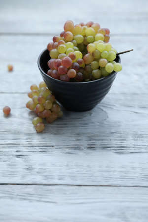 Red green grapes in a black bowl on a gray wooden table.の写真素材