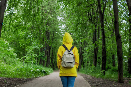 Shot back a young woman in a yellow hoodie stands in the summer forest. Trip in a forest.の写真素材