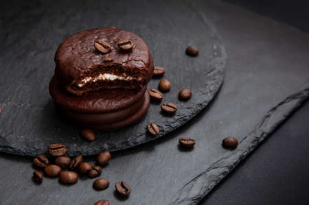 A few sweet Choco pie desserts on a black stone board among scattered coffee beans.Chocolate and...
