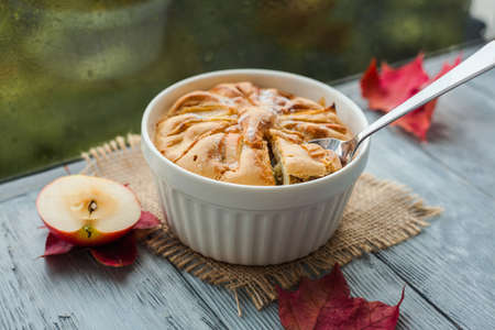 Apple pie in a white bowl on a wooden table near a rainy autumn window.の写真素材