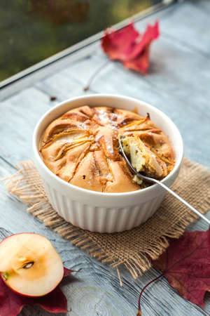 Apple pie in a white bowl on a wooden table near a rainy autumn window.の写真素材