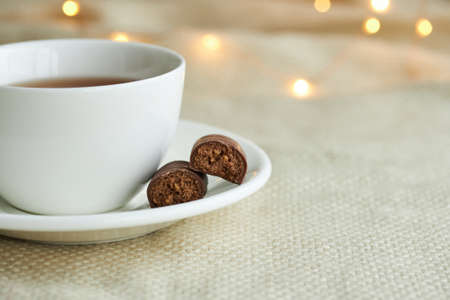 White cup of tea with chocolate sweets on a beige plaid. Christmas lights and copy space.の写真素材