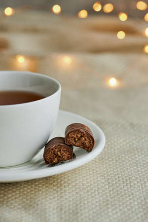 White cup of tea with chocolate sweets on a beige plaid. Christmas lights and copy space.の写真素材