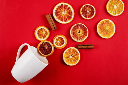 White mug with scattered dried orange slices and cinnamon on a red background. Christmas composition flat lay.の写真素材