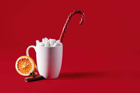 White mug with marshmallows and christmas lollipop on a red background.の写真素材