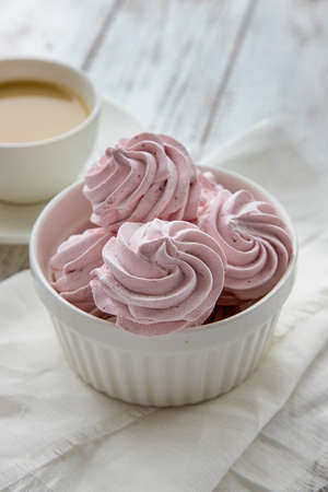 Pink Meringue marshmallow zephyr in a white bowl on a white wooden table.の写真素材
