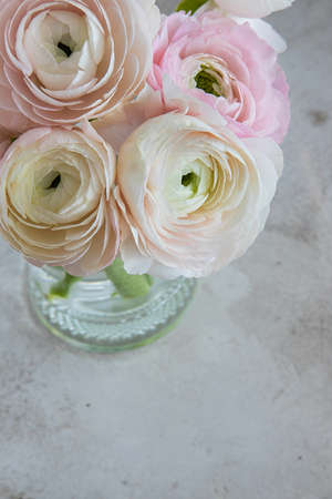 Bouquet of soft pink ranunculus flowers in a glass vase and gray table,top view.