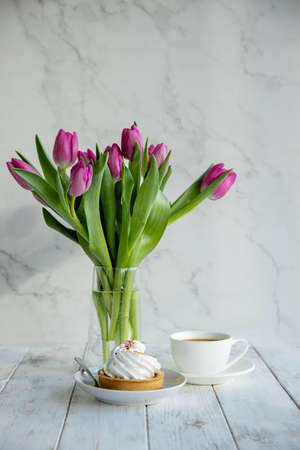 Tulips in a vase and a sweet dessert with a cup of coffee on gray wooden table. Morning romantic...