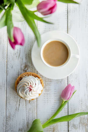 Tulips in a vase and a sweet dessert with a cup of coffee on gray wooden table. Spring breakfast...