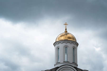 White church with a golden dome and a cross close up against a stormy sky