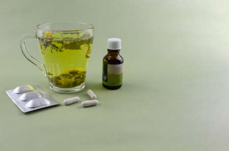 Glass cup with a decoction of herbs on a light background with the other side of the pill and a disposable syringe. Seasonal diseases, alternative medicineの写真素材