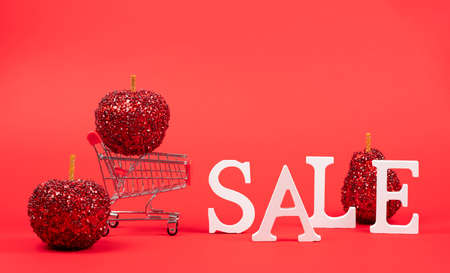 Shopping cart with Christmas decorations standing on a red background. Christmas and New Year sales.の写真素材