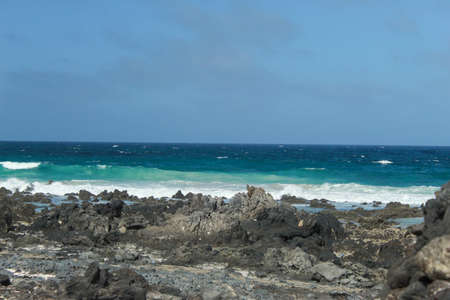 black rocky beach with small waves and clear blue skyの写真素材