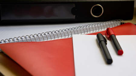 two pen on white paper, a red folder and a black folder