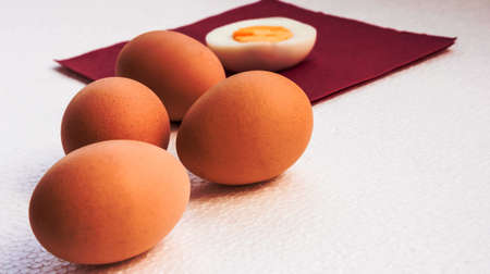 four orange boiled eggs lie on a light uneven surface, a half of the cut egg lies on a napkin of claret color,の写真素材