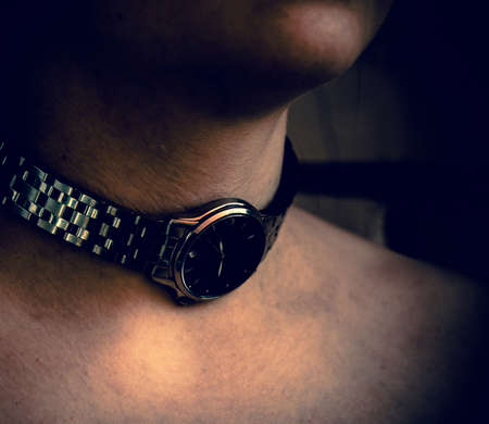 chin and neck of a man in dark processed tones with an iron clock around his neck, profile, background, closeup, figure six on the dialの写真素材