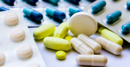 pills in packaging, bright yellow and big white are scattered and lie on a white tableの写真素材